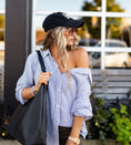 Load image into Gallery viewer, Woman wearing a black cap and striped button down shirt, holding a black bag outdoors. - Thread Vision Spotlight, Hill x Sarah, Sarah Hill