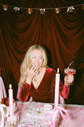 Load image into Gallery viewer, Woman in a red dress sitting at a table with candles and a glass of red wine, and beautiful table decorations and table clothes smiling. Thread Vision Client Spotlight, Maude & May by Talia Hubble