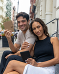 Load image into Gallery viewer, Man and woman sitting together on a city street, holding passport wallets. - Thread Vision Client Spotlight, RESET by Serena Pitt