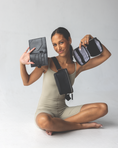 Load image into Gallery viewer, Woman holding a passport wallet and an accessory case, wearing a black fanny pack bag, against a white background - Thread Vision Client Spotlight, RESET by Serena Pitt