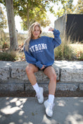 Load image into Gallery viewer, Woman wearing a blue sweatshirt with 'STRONG is sexy' text, sitting outdoors. - Thread Vision Spotlight, Move Like Morgan