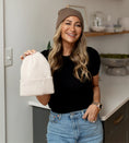 Load image into Gallery viewer, Woman holding a beige beanie in a kitchen setting wearing a mocha, satin-lined beanie - Thread Vision Spotlight, Hill x Sarah, Sarah Hill