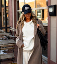 Load image into Gallery viewer, Woman wearing a beige coat and white sweater with a black cap in an outdoor setting. - Thread Vision Spotlight, Hill x Sarah, Sarah Hill 
