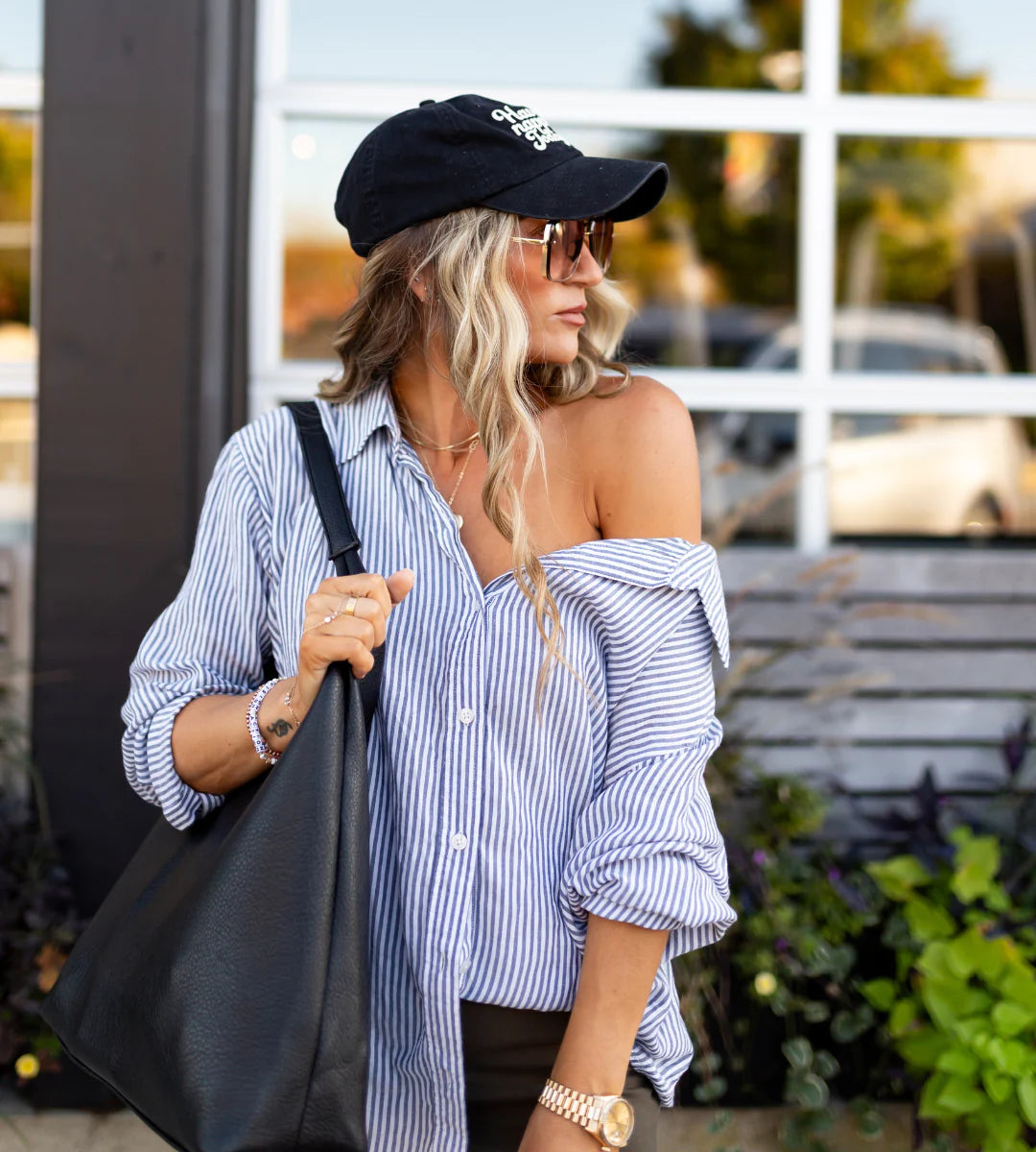 Woman wearing a black cap and striped button down shirt, holding a black bag outdoors. - Thread Vision Spotlight, Hill x Sarah, Sarah Hill 