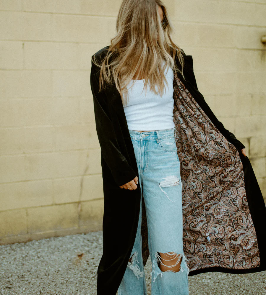 Person wearing a black velvet duster cardigan with a patterned lining, light blue jeans, and a white top against a beige wall. - Thread Vision Spotlight, Hill x Sarah, Sarah Hill 