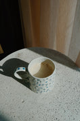Load image into Gallery viewer, Empty coffee cup with blue floral pattern on a concrete surface - Thread Vision Spotlight, Ignited Apparel
