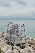 Load image into Gallery viewer, Blue and white patterned bag on rocks with a body of water and sky in the background - Thread Vision Spotlight, Ignited Apparel
