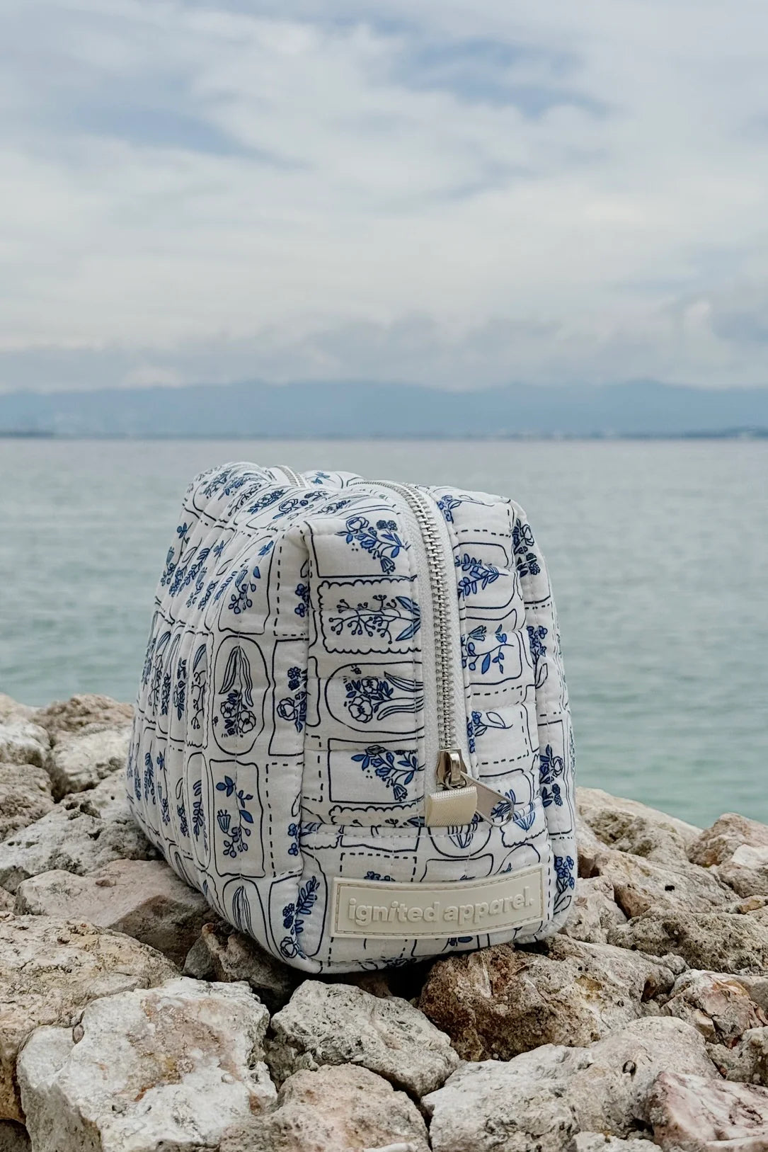 Blue and white patterned bag on rocks with a body of water and sky in the background - Thread Vision Spotlight, Ignited Apparel