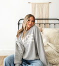 Load image into Gallery viewer, Woman wearing a gray sweatshirt with text, sitting on a bed in a cozy room. - Thread Vision Spotlight, Hill x Sarah, Sarah Hill 
