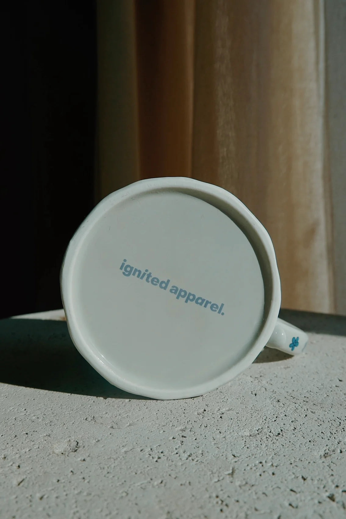 White mug with 'ignited apparel.' branding on a concrete surface. - Thread Vision Spotlight, Ignited Apparel