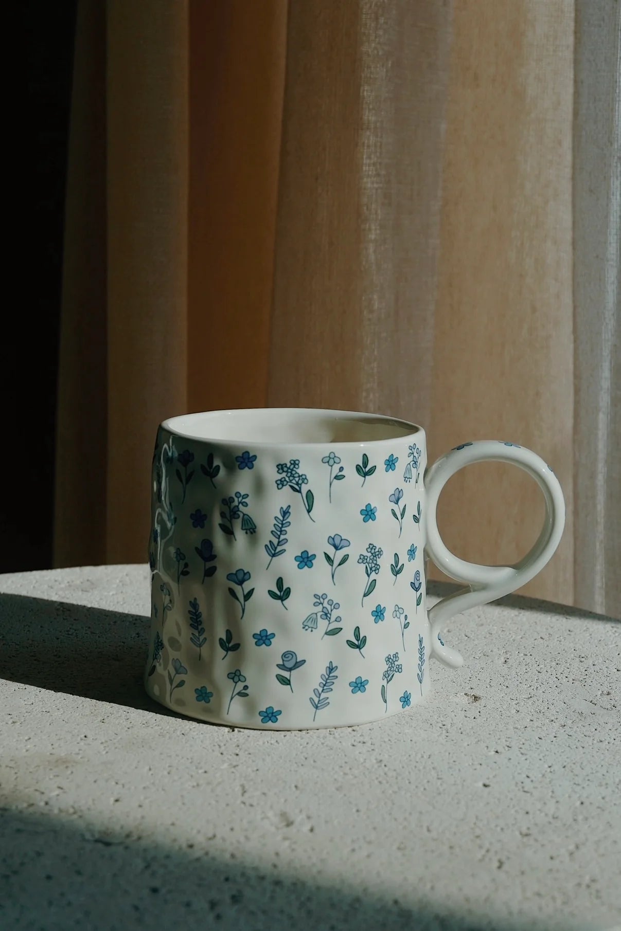 White ceramic mug with floral pattern on a concrete surface with striped wall in the background - Thread Vision Spotlight, Ignited Apparel