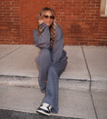 Load image into Gallery viewer, Person wearing a gray outfit sitting on a sidewalk with a brick wall background - Thread Vision Spotlight, Hill x Sarah, Sarah Hill 
