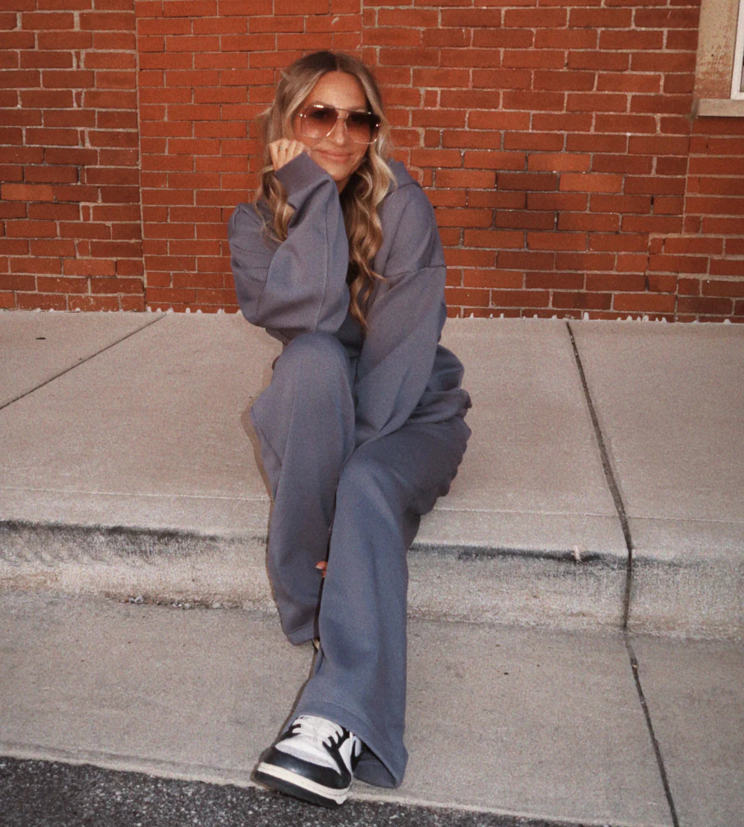 Person wearing a gray outfit sitting on a sidewalk with a brick wall background - Thread Vision Spotlight, Hill x Sarah, Sarah Hill 