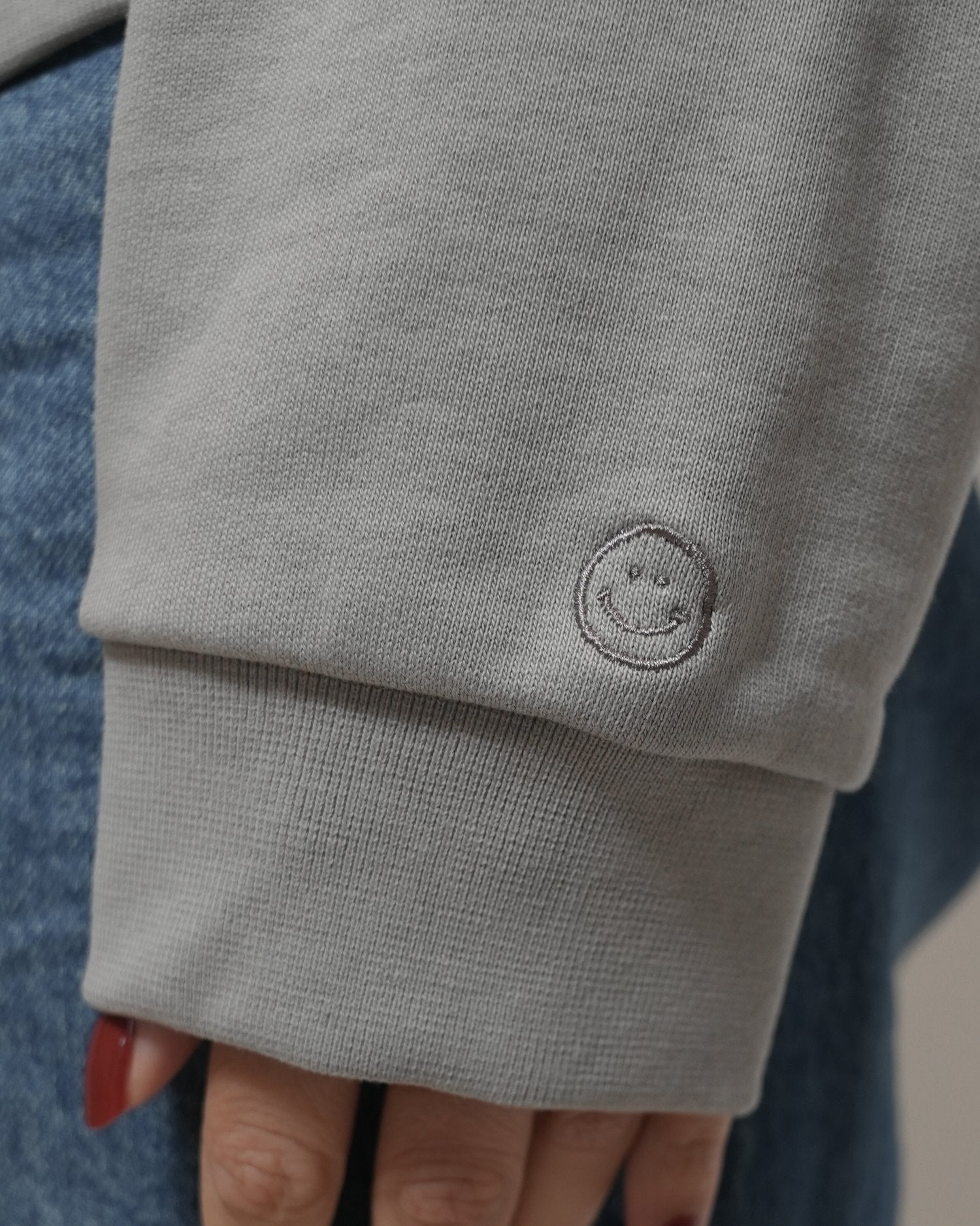 Close-up of a gray sweatshirt with a smiley face emblem on the sleeve. - Thread Vision Spotlight, Loe Hayley