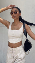 Load image into Gallery viewer, Woman wearing a white top and beige pants with sunglasses and a black handbag against a plain background Woman in a white outfit standing against a white wall.  - Thread Vision Client Spotlight, Asha Bailey
