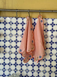 Load image into Gallery viewer, Pink embroidered cloths hanging on a rack against a patterned wall. Thread Vision Client Spotlight, Maude & May by Talia Hubble
