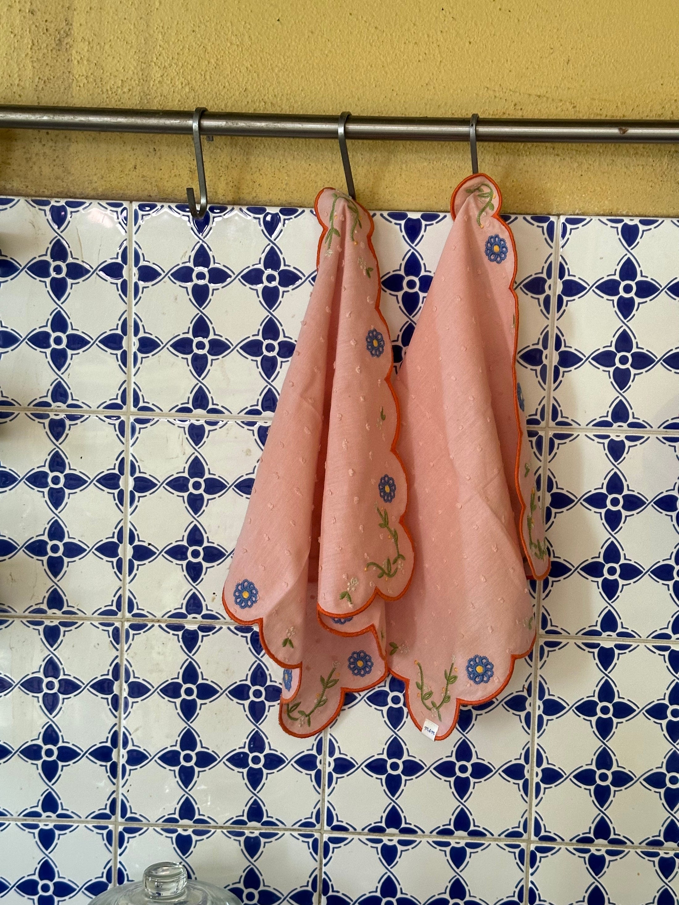 Pink embroidered cloths hanging on a rack against a patterned wall. Thread Vision Client Spotlight, Maude & May by Talia Hubble