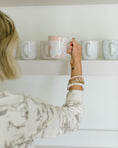 Load image into Gallery viewer, Person holding a pink mug with other mugs on a shelf in the background - Thread Vision Spotlight, Loverly Grey
