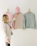 Load image into Gallery viewer, Woman selecting a pink beanie from three sweaters on hangers against a white wall. - Thread Vision Spotlight, Loverly Grey

