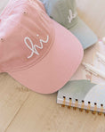 Load image into Gallery viewer, Pink cap with 'hi' embroidery on a wooden surface with a notebook and pen. - Thread Vision Spotlight, Loverly Grey
