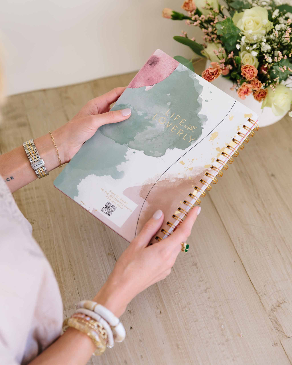 Person holding a spiral-bound notebook with floral design on a wooden surface - Thread Vision Spotlight, Loverly Grey
