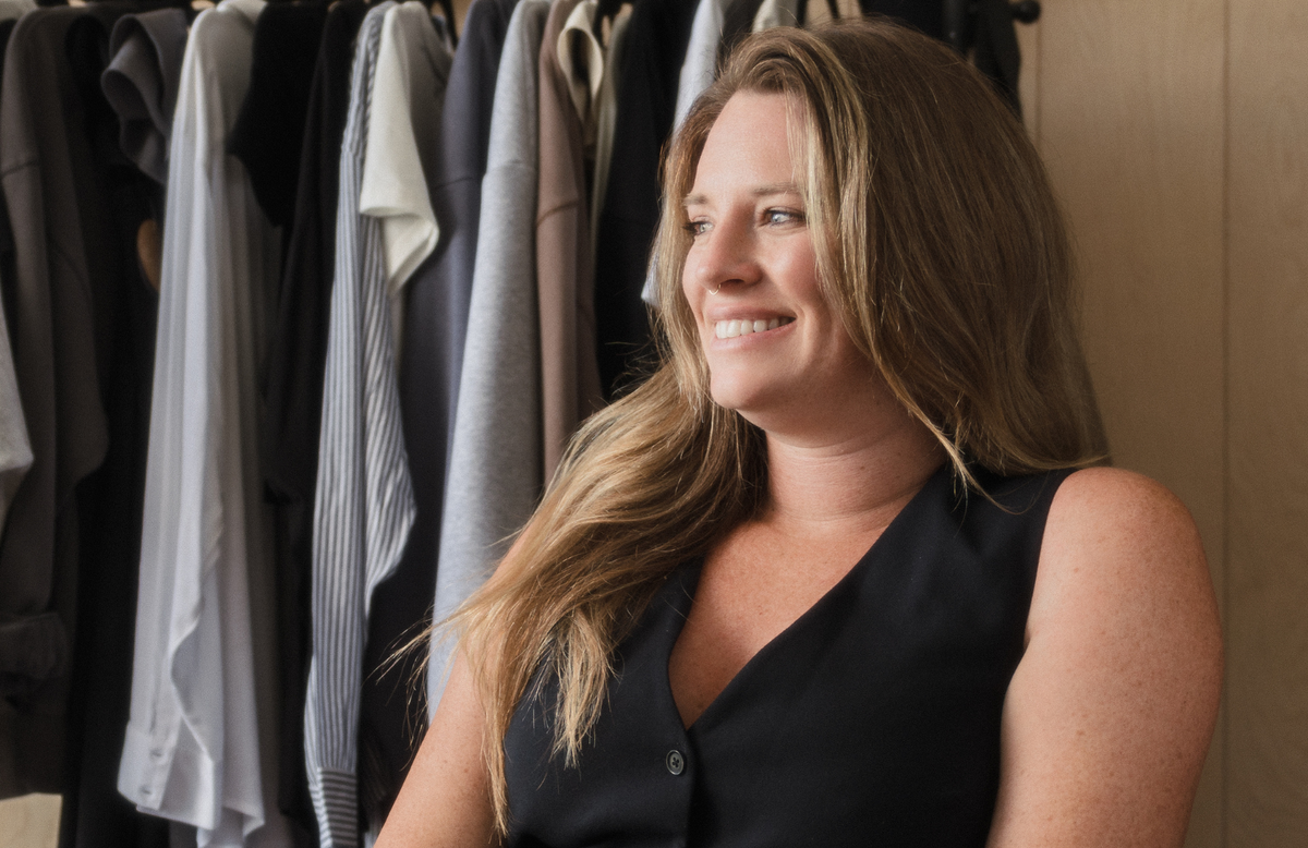 Woman standing in front of a rack of clothes, smiling. - - Thread Vision Branded Photo 