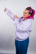 Load image into Gallery viewer, Person wearing a light purple hoodie with a logo, holding a matching shirt against a plain background - Thread Vision Client Spotlight, 10/10 Deanna Giulietti 
