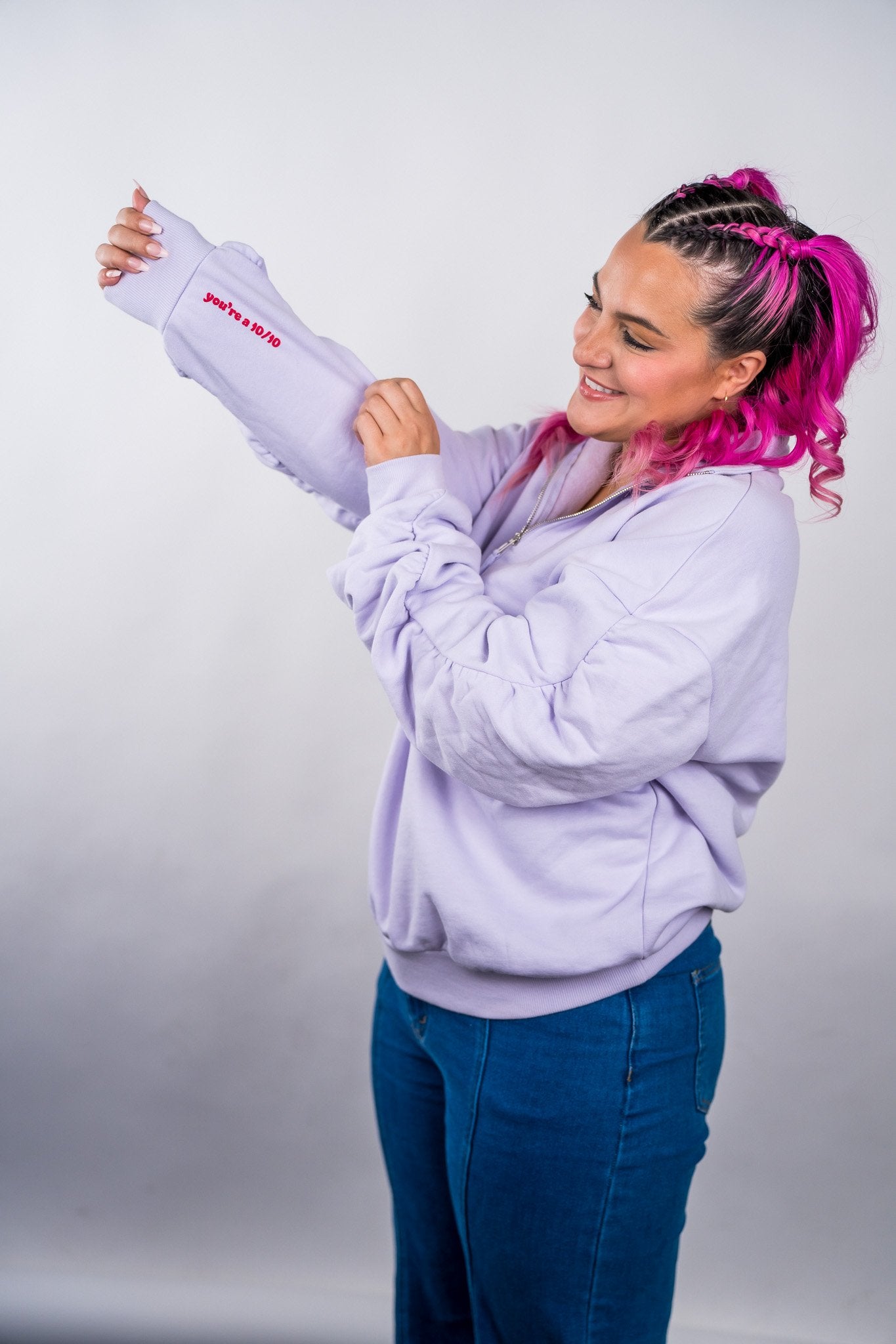 Person wearing a light purple hoodie with a logo, holding a matching shirt against a plain background - Thread Vision Client Spotlight, 10/10 Deanna Giulietti 