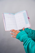 Load image into Gallery viewer, Hand holding an open planner with a teal sleeve on a gray background - Thread Vision Client Spotlight, 10/10 Deanna Giulietti 
