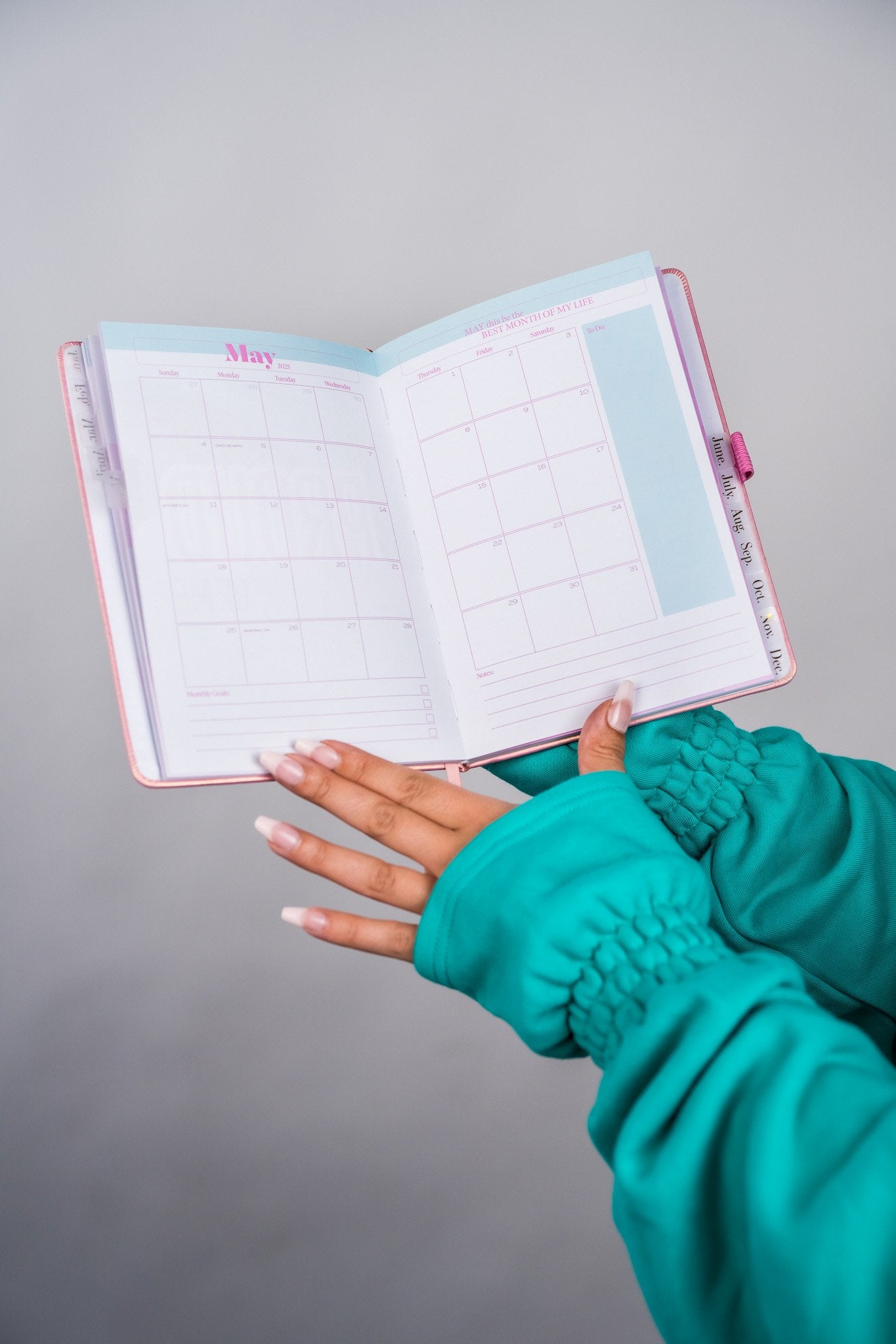 Hand holding an open planner with a teal sleeve on a gray background - Thread Vision Client Spotlight, 10/10 Deanna Giulietti 