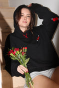 Load image into Gallery viewer, Person wearing a black hoodie with red floral designs, holding flowers indoors. - Thread Vision Client Spotlight, Sunday Cherries
