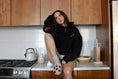 Load image into Gallery viewer, Person sitting on a kitchen counter wearing a black hoodie with red accents. - Thread Vision Client Spotlight, Sunday Cherries
