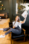 Load image into Gallery viewer, Woman sitting in a chair holding three notebooks in a cozy room with plants and furniture. - Thread Vision Client Spotlight, Skinny Hangover
