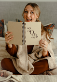 Load image into Gallery viewer, Woman holding a notebook with '2021' on it, sitting on a bed. - Thread Vision Client Spotlight, Skinny Hangover
