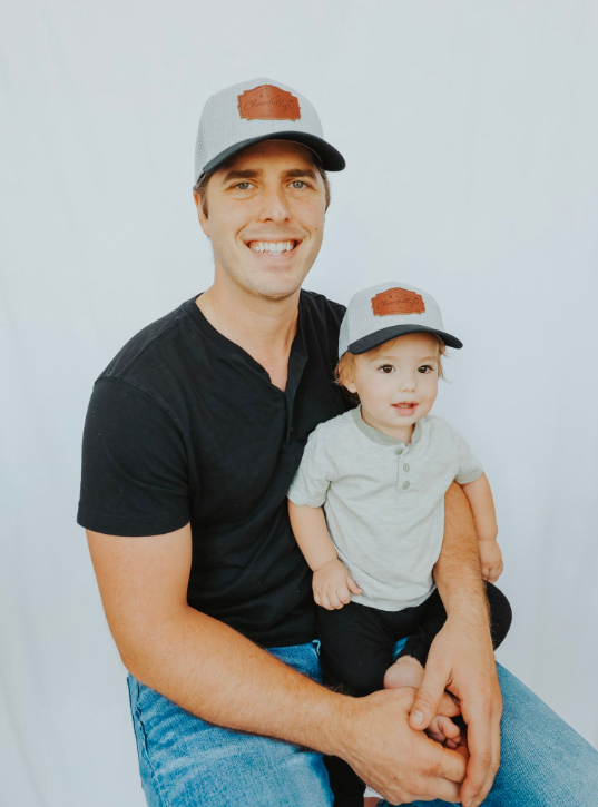 Man holding a child both wearing baseball caps against a plain background Thread Vision, Client Cheerfully U