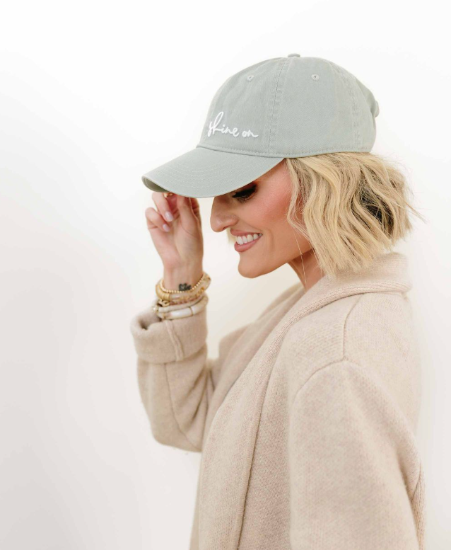 Woman wearing a light gray cap with text, smiling against a white background Thread Vision, Client Loverly Grey