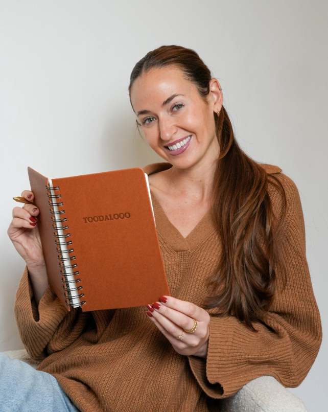 Woman holding a brown notebook with 'TOODALOO' branding against a plain background - Thread Vision, Client Loe Haley