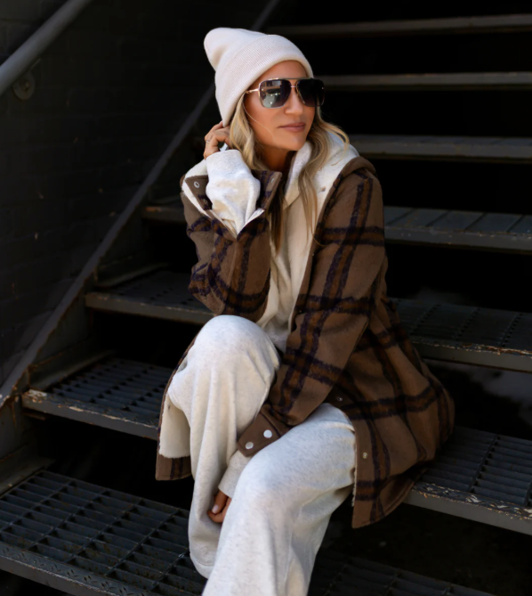 Person wearing a plaid coat, white beanie, and sunglasses sitting on stairs.   Thread Vision, Client Sarah Hill, Hill x Sarah
