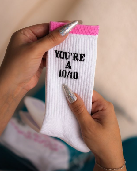 White sock with text held by a hand against a neutral background   Thread Vision, Client 10/10 Deanna Giulietti