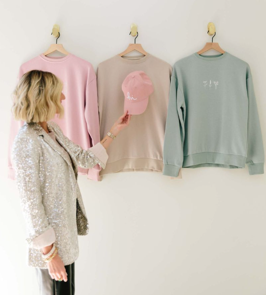 Woman looking at three sweaters on hangers against a white wall -  - Thread Vision, Client Loverly Grey