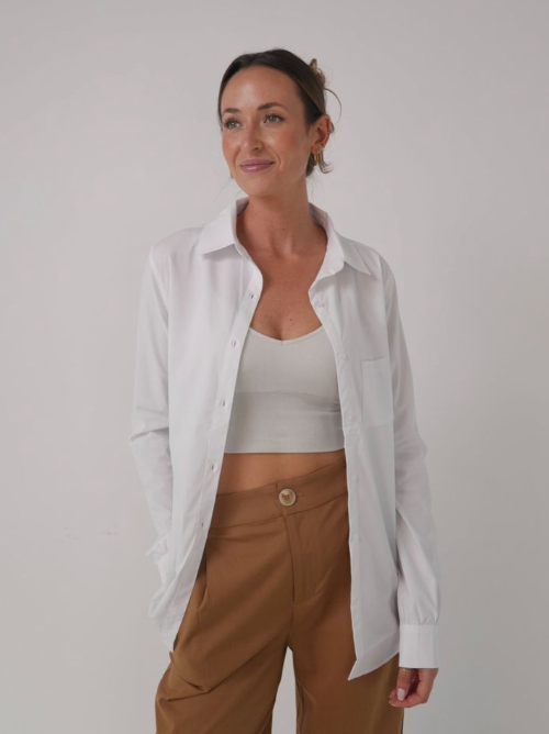 Woman wearing a white shirt over a white top and brown pants on a plain background -  - Thread Vision, Client Loe Haley