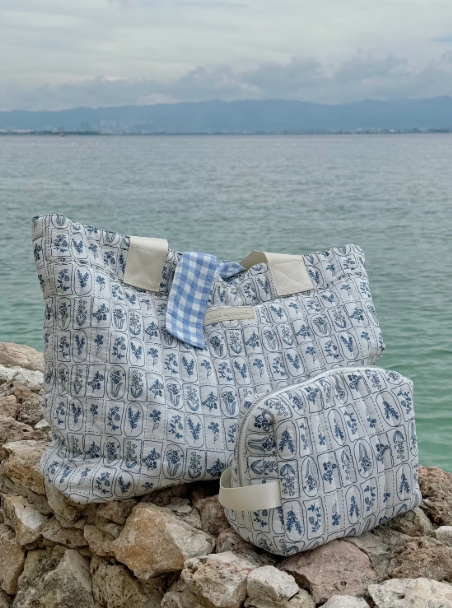 Floral-patterned bags on rocks with a body of water and mountains in the background -  - Thread Vision, Client Ignited Apparel