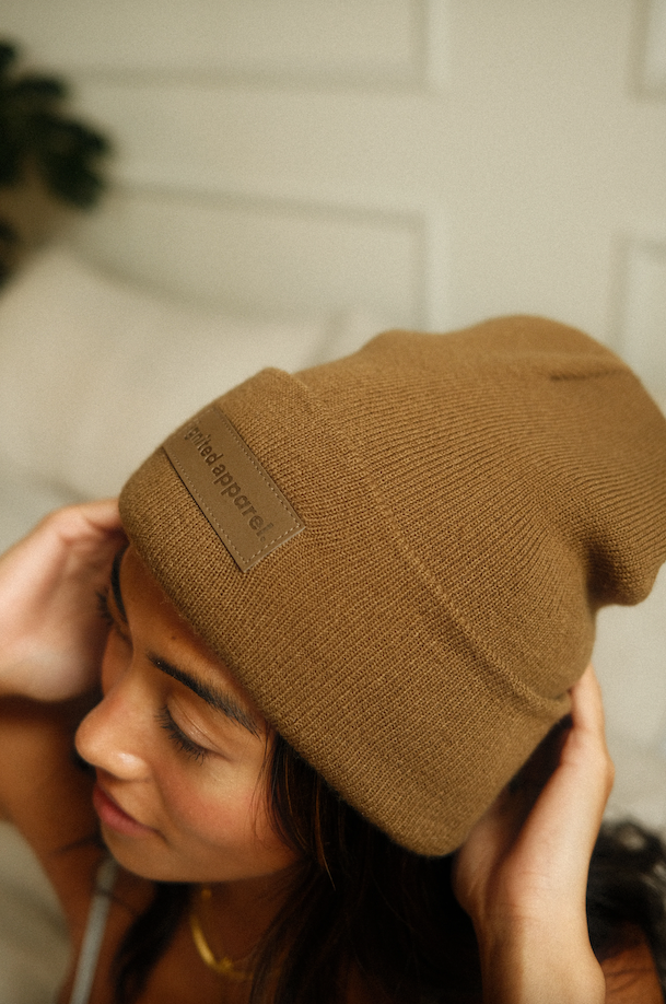 Person wearing a brown beanie with a brand tag against a neutral background - Thread Vision Spotlight, Ignited Apparel