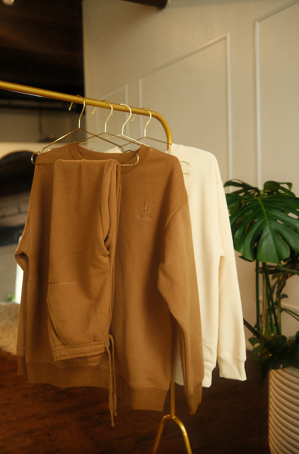 Brown and beige shirts hanging on a gold rack with a plant in the background. - Thread Vision Spotlight, Ignited Apparel