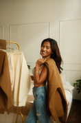 Load image into Gallery viewer, Woman holding a brown sweatshirt standing in a room with clothing racks. - Thread Vision Spotlight, Ignited Apparel
