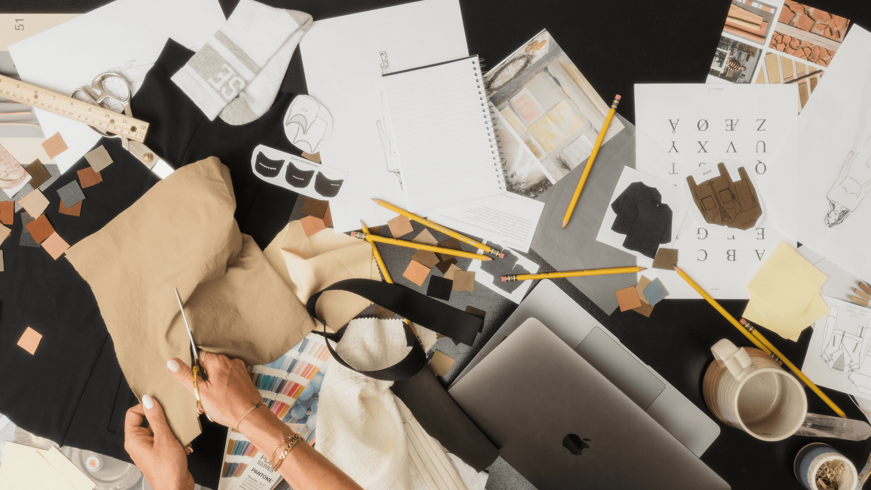 Design workspace with laptop, sketches, and materials on a table - Thread Vision Branded Photo 