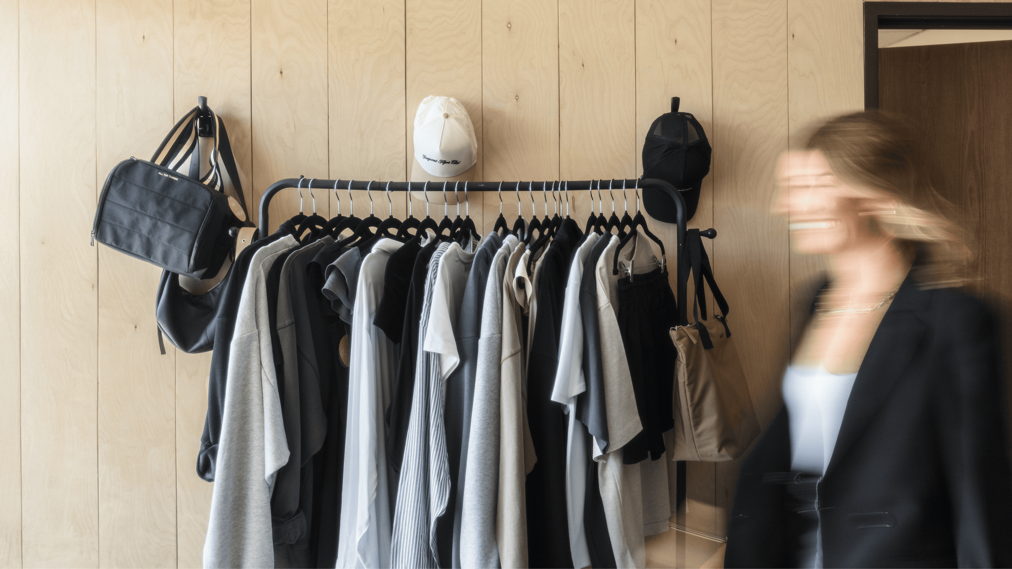 Clothing rack with shirts and bags against a wooden wall, blurred person in foreground - - Thread Vision Branded Photo 