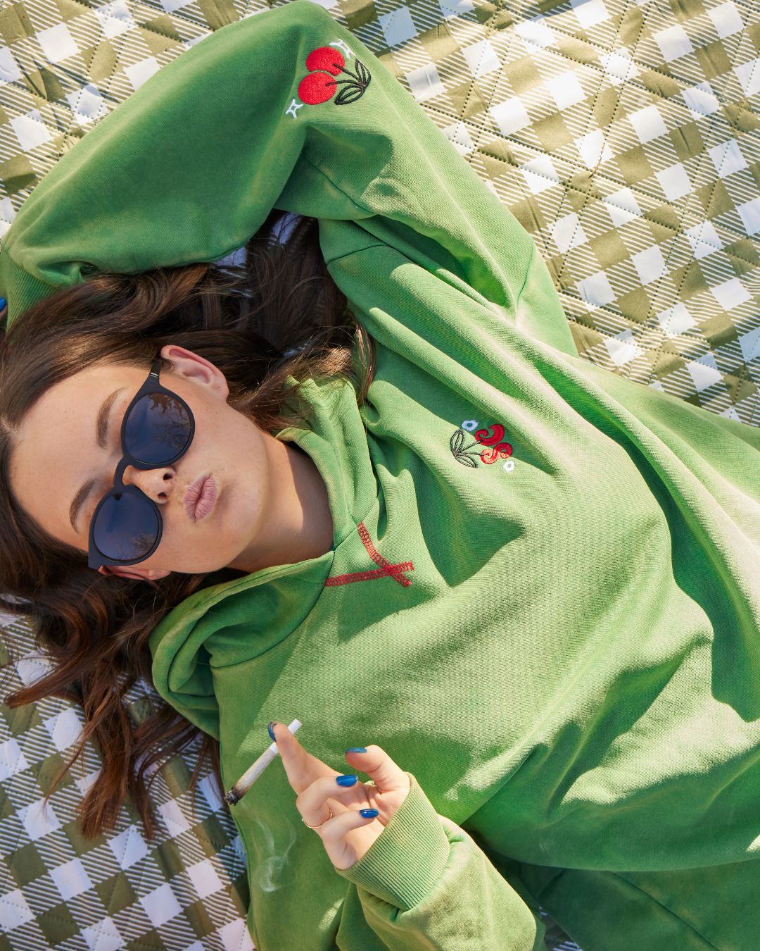 Person wearing a green hoodie with cherry designs, lying on a checkered surface. - - Thread Vision Client Spotlight, Sunday Cherries