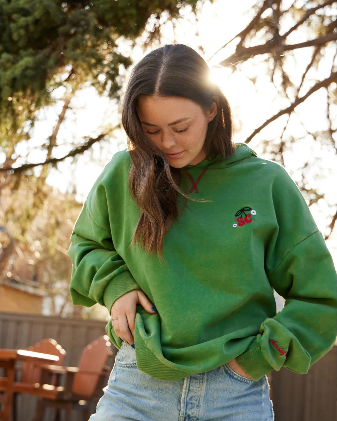 Person wearing a green hoodie with a small design, standing outdoors with trees in the background. - Thread Vision Client Spotlight, Sunday Cherries