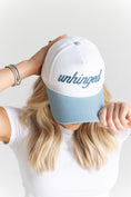 Load image into Gallery viewer, Person holding a white and blue cap with 'unhinged' text against a light background - Thread Vision Spotlight, Move Like Morgan
